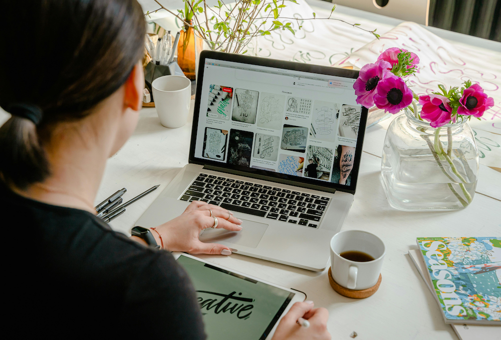 Back of a female who is working on her laptop with a vase of pink flowers beside her