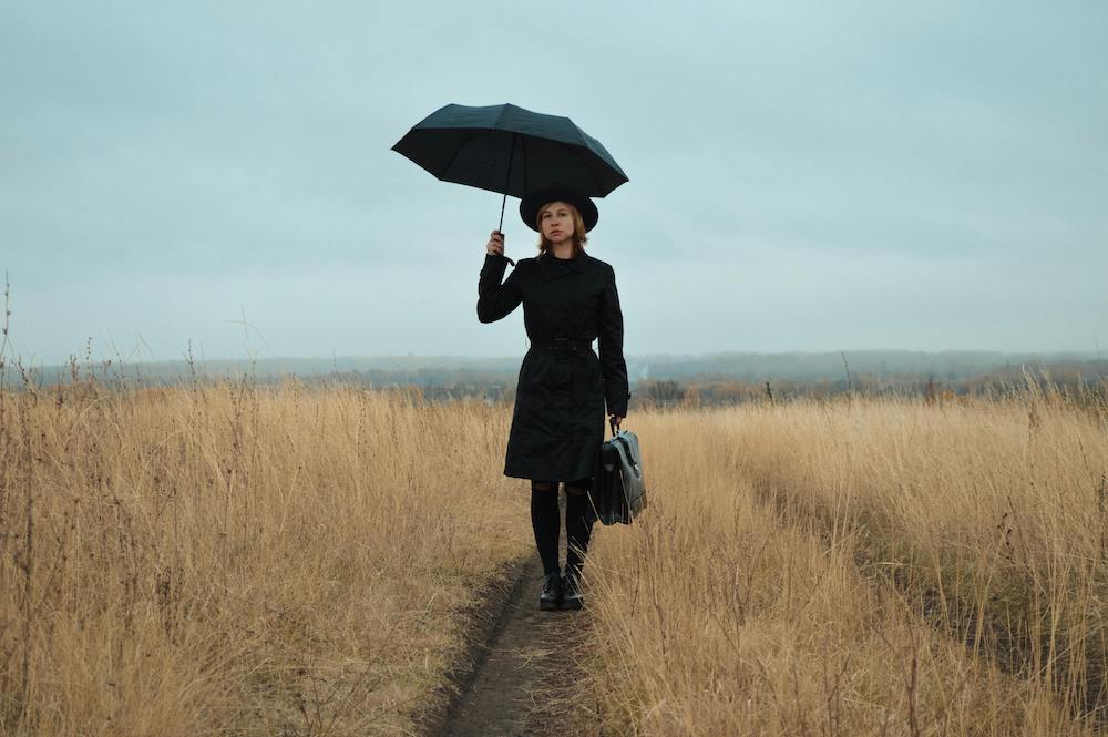 woman in a field in a business suit with an umbrella and briefcase