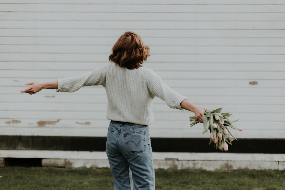 Woman with arms wide holding a bunch of tulips with a background of white weatherboards.