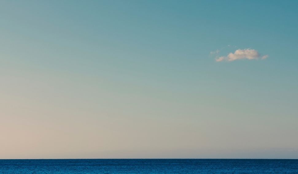 Blue sky with small white cloud and still ocean
