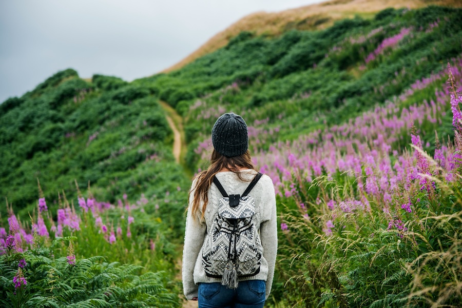 Woman hiking along a mountain track with pink flowers.
