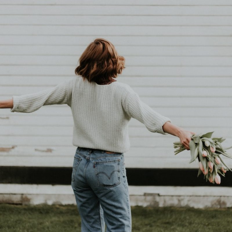 Woman with arms wide holding a bunch of tulips with a background of white weatherboards.