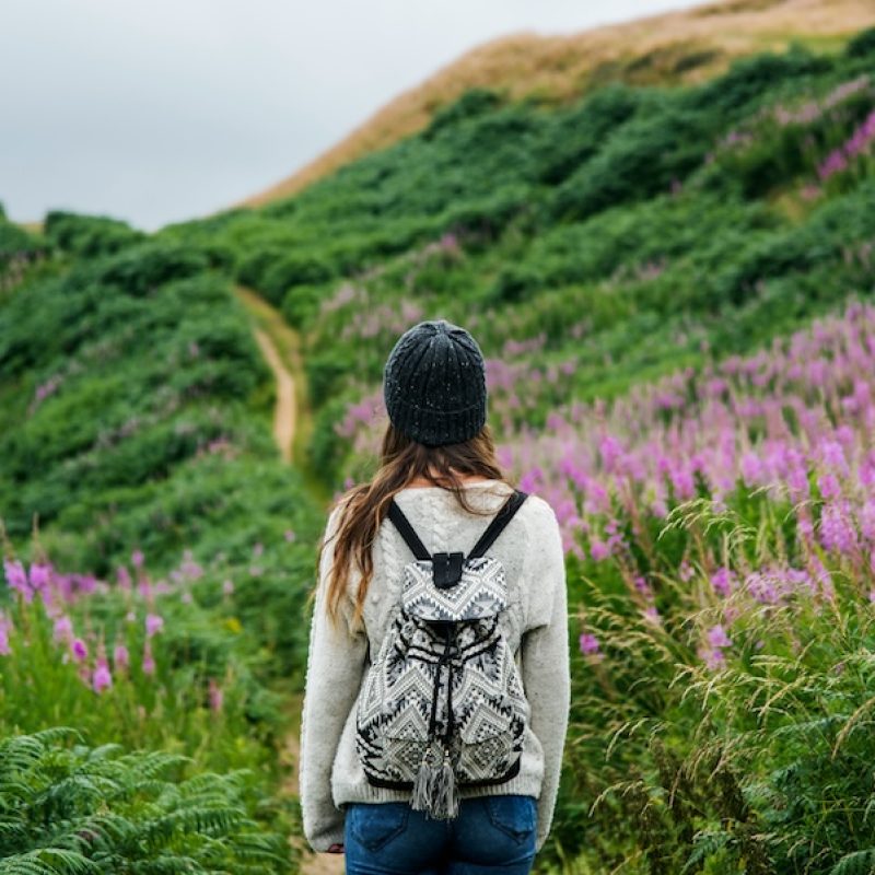 Woman hiking along a mountain track with pink flowers.