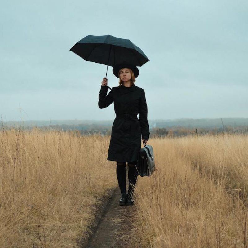 woman in a field in a business suit with an umbrella and briefcase