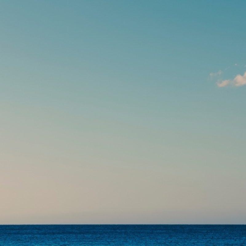 Blue sky with small white cloud and still ocean