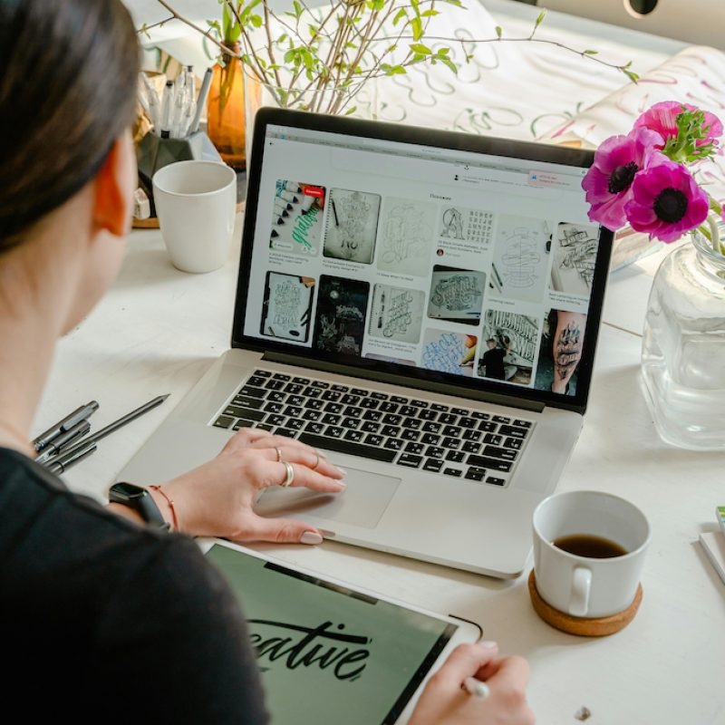 Back of a female who is working on her laptop with a vase of pink flowers beside her