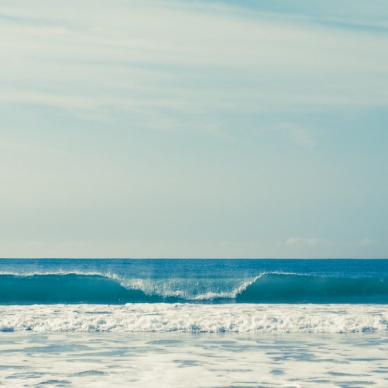Wave breaking with horizon and soft clouds in the background.